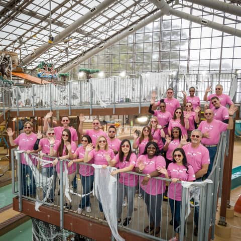 A group of volunteers standing in an indoor water park facility and waving at the camera.